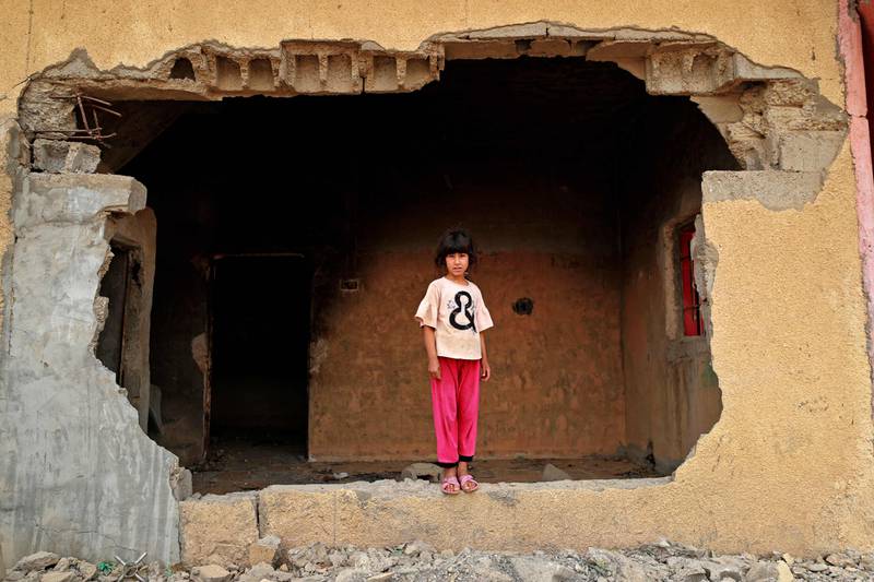 A girl stands on the wall of her family's damaged house. 