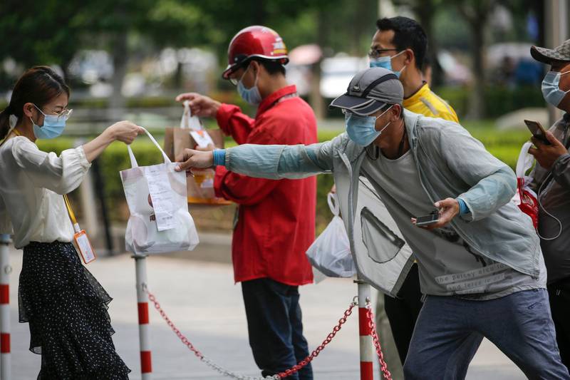 A food delivery man passes a food pack to a masked woman outside an office building in Beijing, China. AP Photo