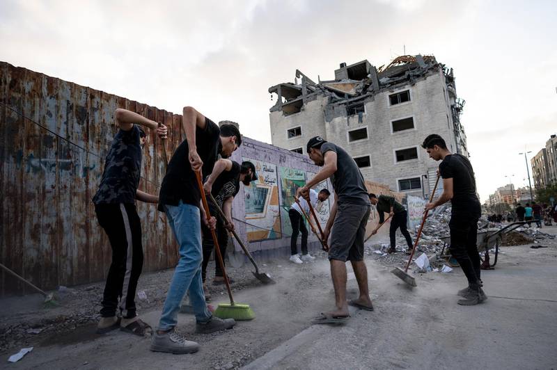 People clean the streets of debris beside a building that was damaged in an air strike after the end of an 11-day war between Gaza's Hamas rulers and Israel, in Gaza City. AP Photo