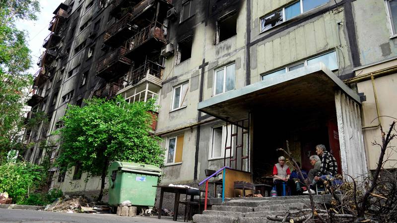 Residents sit outside a destroyed apartment building in Mariupol. AFP