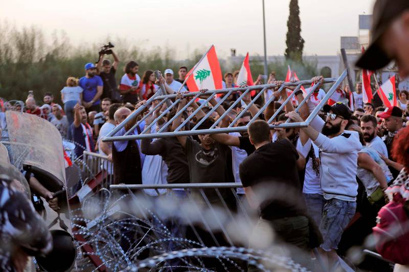 Lebanese demonstrators try to remove the barbed-wire and metal rail, placed by anti-riot police (background), on the road leading to the Presidential Palace in Baabda, on the eastern outskirts of Beirut on November 13, 2019, nearly a month into an unprecedented anti-graft street movement. Street protests erupted, the night before, after President Michel Aoun defended the role of his allies, the Shiite movement Hezbollah, in Lebanon's government. Protesters responded by cutting off several major roads in and around Beirut, the northern city of Tripoli and the eastern region of Bekaa. / AFP / ANWAR AMRO
