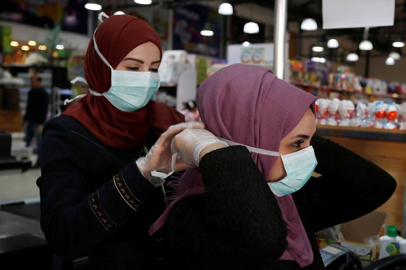 A Palestinian cashier is helped by her colleague to put on a mask amid coronavirus precautions, in a supermarket in Gaza City March 8, 2020. Reuters