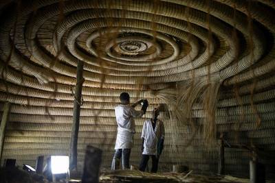 Traditional artisans fix the circular rings in the ceiling of a building in the Kasubi Royal Tombs.