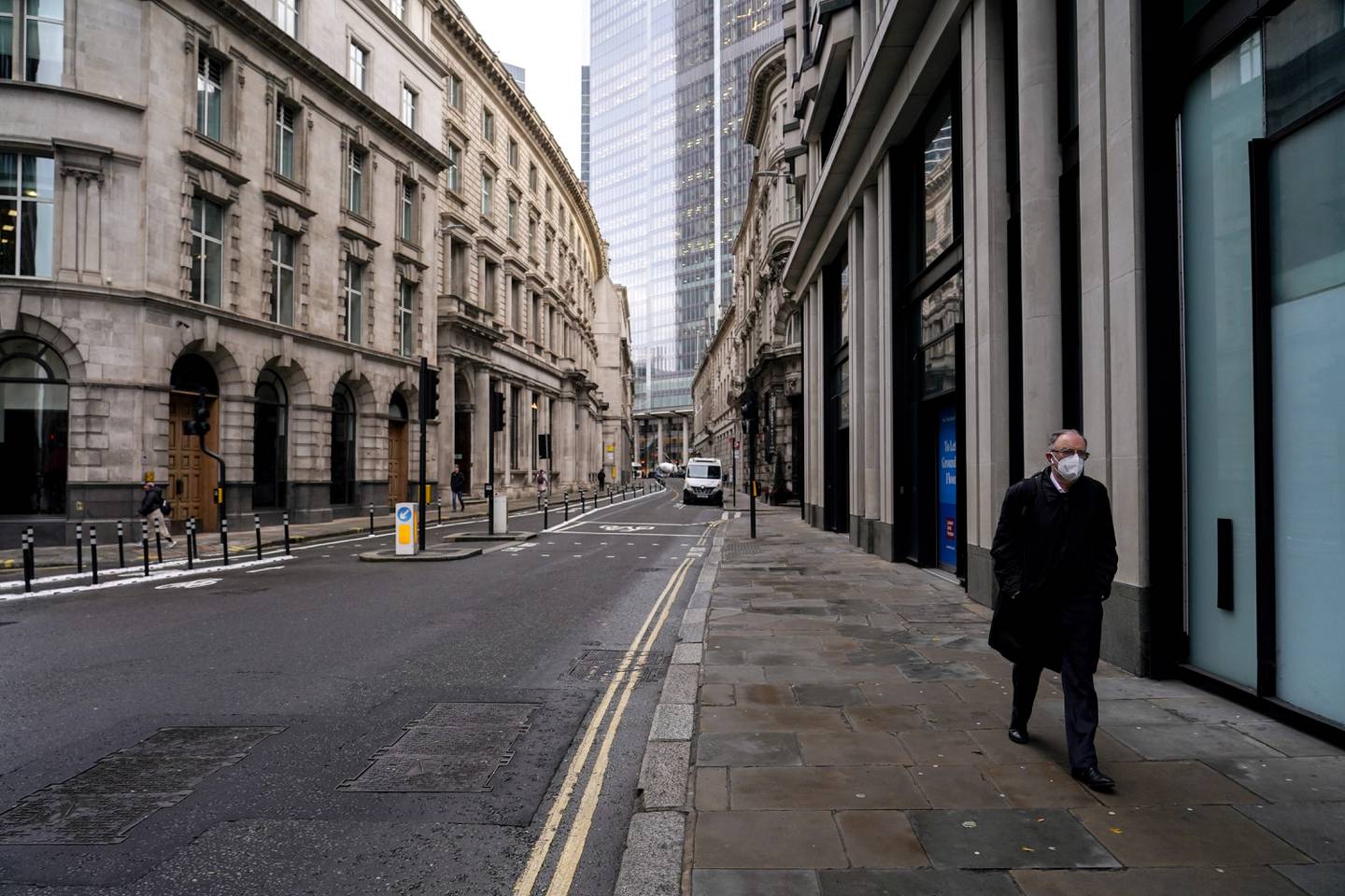 A man wears a face mask while walking in an empty street in the London's financial district, known as The City, as new work from home guidance came into effect. AP.