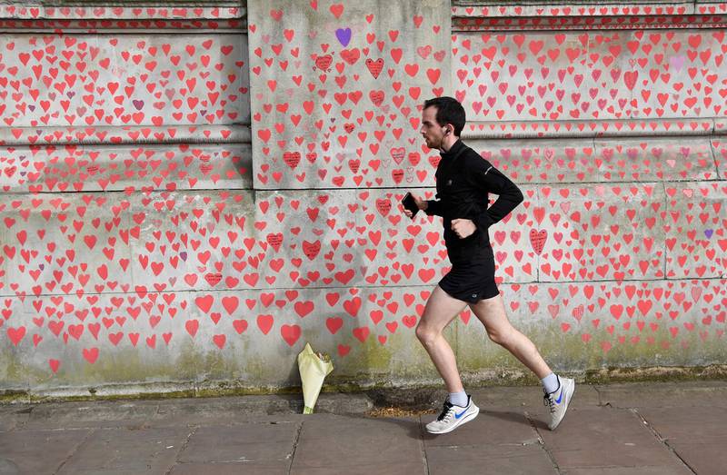 A man runs past a wall of hearts being painted by volunteers and relatives of bereaved beside St Thomas' hospital as a memorial to all those who have died so far in the UK from Covid-19 in London, Britain, April 1, 2021. Reuters