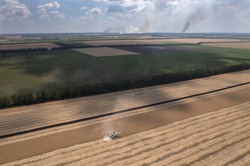 Smoke rises in the background as a farmer harvests a field in the Dnipropetrovsk region of Ukraine. AP