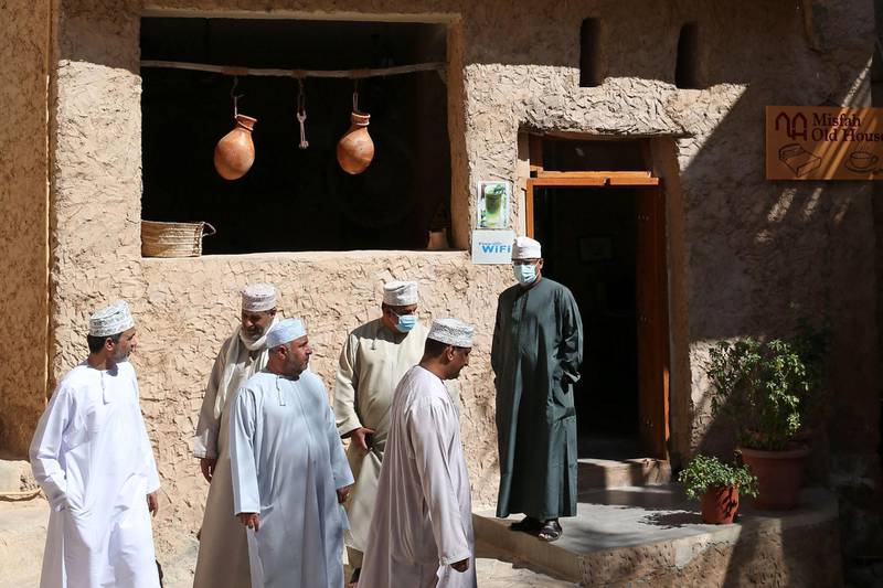 Locals stand outside a boutique hotel in the village of Misfat al-Abriyeen which opened its narrow streets six years ago to foreigners and locals seeking adventure in the deserts and green corners of the Gulf sultanate of Oman, on February 8, 2021. Perched on an Oman mountain top, the village of Misfat al-Abriyeen has changed its fortunes by transforming mud-brick homes into boutique hotels, drawing tourists to a region famed for hiking trails and tales of genies. / AFP / MOHAMMED MAHJOUB
