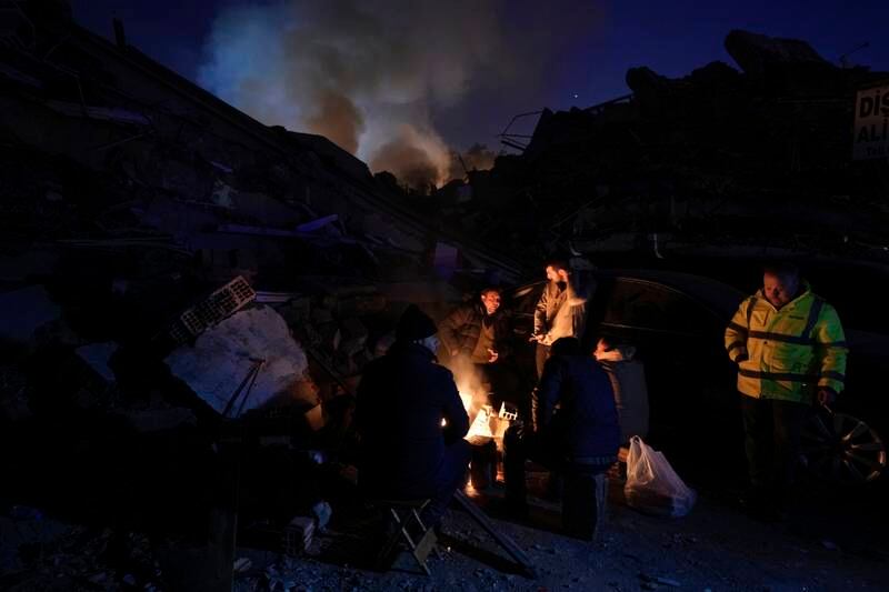 People warm up with fire in front of destroyed buildings. AP 