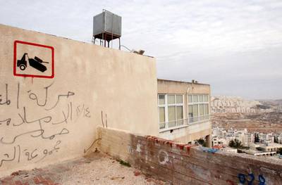 epa01191062 Illusive British graffiti artist named Banksy has painted new works in the West Bank town of Bethlehem, which might include a stencil of a tank being towed away, executed on the wall of a house on a main street in Bethlehem, on 04 December 2007. Behind is the large Jewish settlement called Har Homa, still under construction. Banksy's identity is not known and his works are not signed.  EPA/JIM HOLLANDER *** Local Caption *** 01191062
