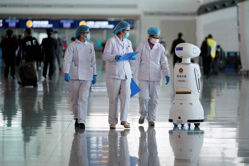 Medical workers walk by a police robot at the Wuhan Tianhe International Airport. Reuters