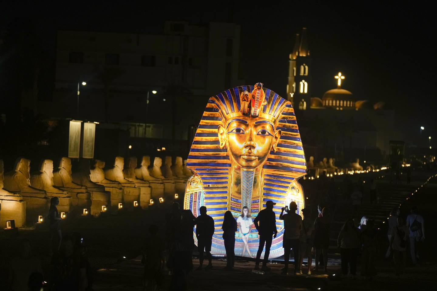 Tourists stand by a model of the golden mask of King Tutankhamun, on the Avenue of Sphinxes in Luxor, on Friday. AP