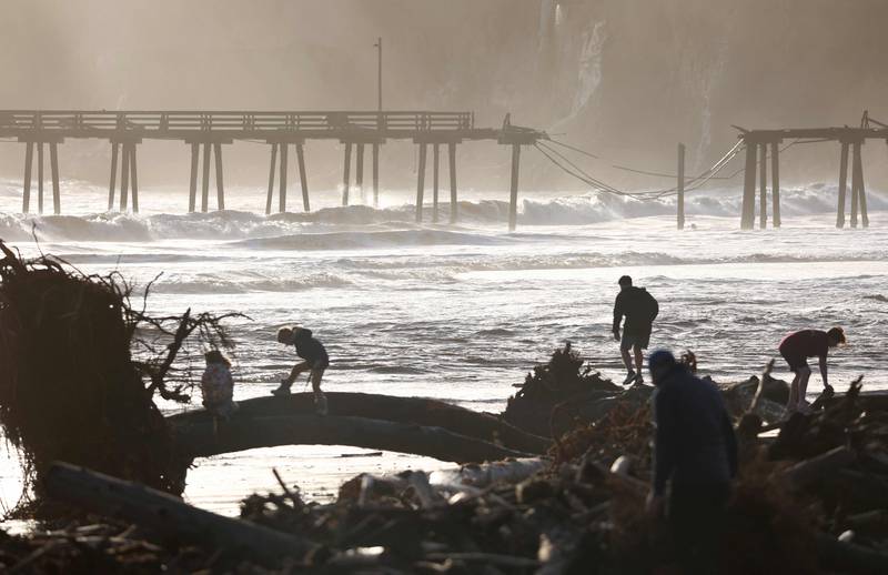 People look at storm debris on the beach, with a storm-damaged pier in the background, in Capitola. Getty / AFP