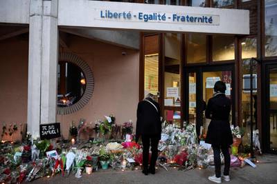 People look at flowers at the entrance of a middle school in Conflans-Sainte-Honorine, 30kms northwest of Paris, on October 17, 2020, after a teacher was decapitated by an attacker who has been shot dead by policemen.  The man suspected of beheading on October 16 ,2020 a French teacher who had shown his students cartoons of the prophet Mohammed was an 18-year-old born in Moscow and originating from Russia's southern region of Chechnya, a judicial source said on October 17. Five more people have been detained over the murder on October 16 ,2020 outside Paris, including the parents of a child at the school where the teacher was working, bringing to nine the total number currently under arrest, said the source, who asked not to be named. The attack happened at around 5 pm (1500 GMT) near a school in Conflans-Sainte-Honorine, a western suburb of the French capital. The man who was decapitated was a history teacher who had recently shown caricatures of the Prophet Mohammed in class. / AFP / Bertrand GUAY
