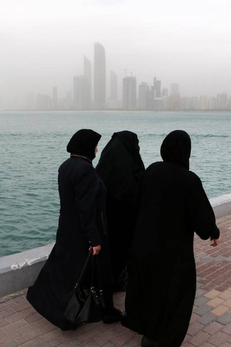 Women walk along the Abu Dhabi Breakwater with a skyline shrouded in fog as rain and wind swept parts of the country on Tuesday. Christopher Pike / The National