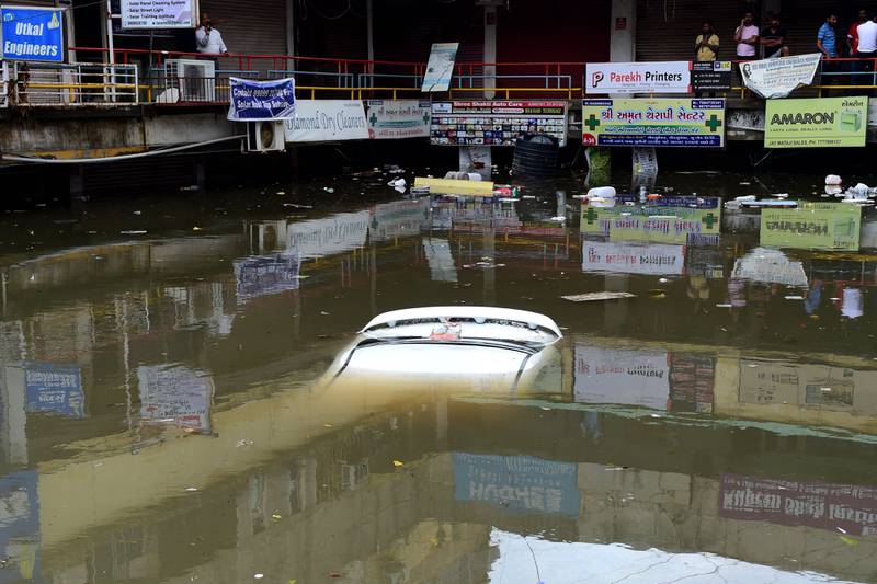 People look at a submerged car in a flooded commercial complex after heavy rains in Ahmedabad. AFP