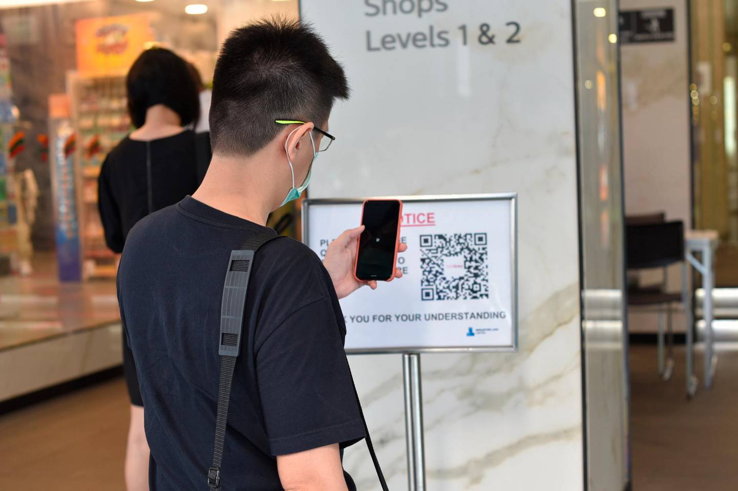 A man scans a QR code before entering a building in Singapore Tuesday, June 2, 2020. Singapore reopened 75 percent of its economy Tuesday, as part of a three-phase controlled approach to end a virus lockdown since early April. (AP Photo/YK Chan)