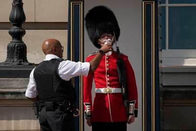 A police officer gives water to a sentry in heavy ceremonial uniform, outside Buckingham Palace in central London. AP