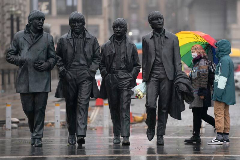 Members of the public wearing face masks stand near a statue of The Beatles in Liverpool. AP Photo