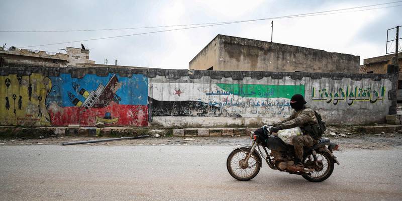 A Syrian man in military fatigues rides a motorbike by a mural-covered wall in the deserted city of Kafranbel. AFP