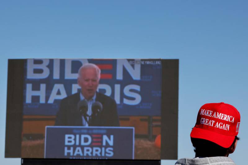 A person wearing a 'Make America Great Again' cap stands in front of a screen showing Democratic U.S. presidential nominee and former Vice President Joe Biden.  Reuters
