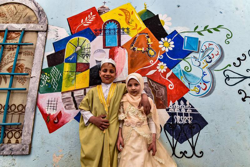 Children pose for a photo in front of a large graffiti depicting cultural elements including mosques, churches, old window lattices of the old town of Iraq's northern city of Mosul, on the first night of the Muslim holy fasting month of Ramadan, during a celebration hosted by a local cultural NGO.  AFP