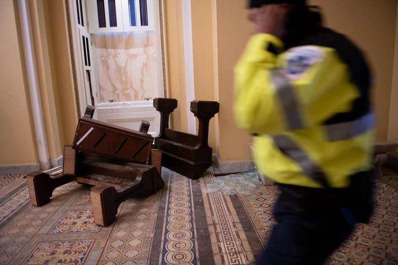 A US Capitol police officer passes in front broken furniture and shattered glass at the Capitol building. Bloomberg
