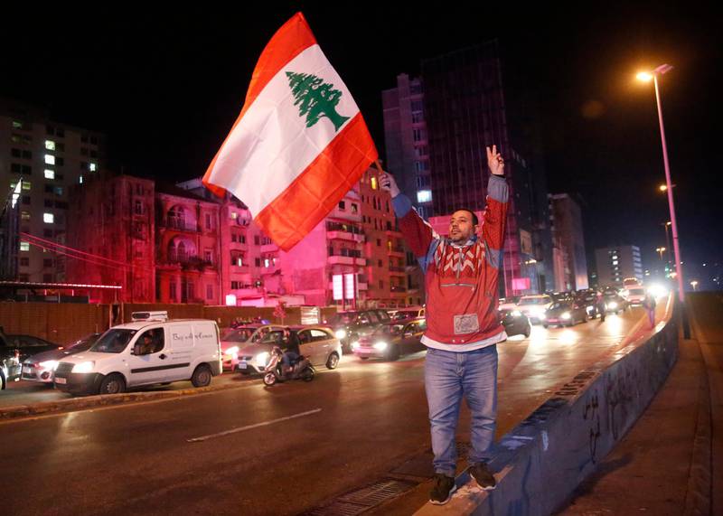 An anti-government protester flashes the victory sign and waves a Lebanese flag, as other protesters block a main road during ongoing protests against corruption and financial crisis, in Beirut, Lebanon.  AP