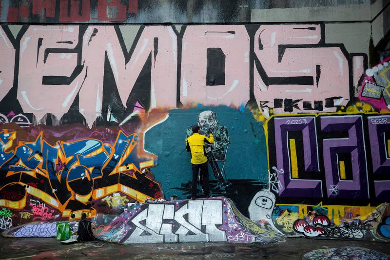 Kevin Belyk paints a mural inspired by a photo of US Senator Bernie Sanders bundled up and wearing mittens and a face mask at President Joe Biden's inauguration, on a legal graffiti wall at the Leeside Tunnel skateboard park in Vancouver, British Columbia.  AP