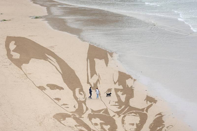 An incoming tide washes away a part of a giant beach sand artwork depicting the faces of the G7 leaders at Watergate Bay Beach, Newquay. Reuters