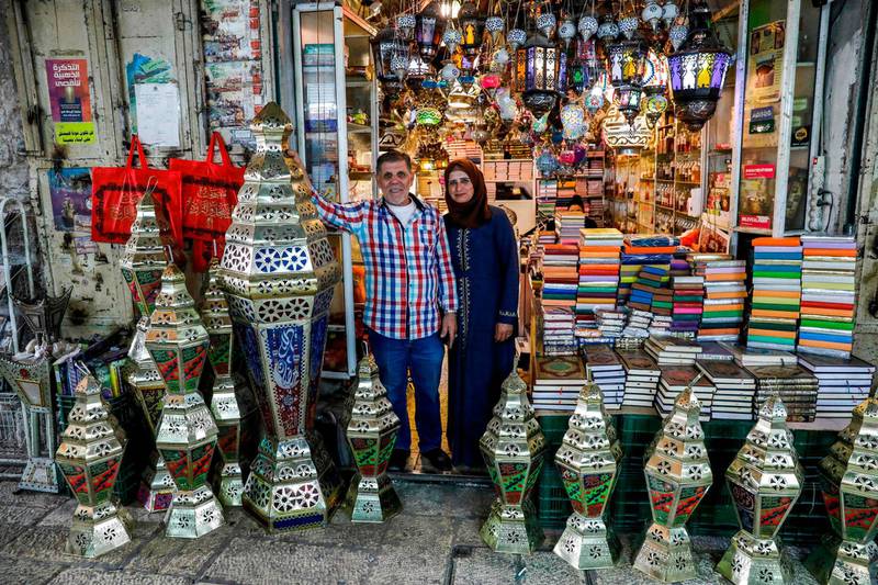 Palestinian craftsman Issam Zughair stands with his wife next to an assortment of Ramadan lanterns in the entrance of his shop in the old city of Jerusalem on May 2, 2019. In his shop in Jerusalem's Old City, Zughair makes traditional lanterns for Muslims marking the holy month of Ramadan, battling competition from cheap Chinese imports. The shop boasts a mix of large and small lamps on show, some hanging from the ceiling while others are displayed outside to draw the attention of passers-by during the lively Ramadan evenings. / AFP / AHMAD GHARABLI

