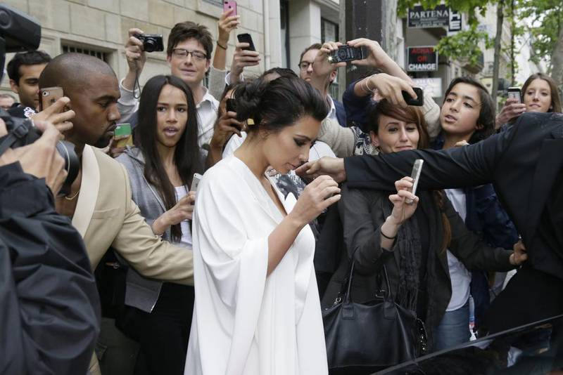 People gather around Kim Kardashian, centre, and Kanye West, left, as they leave their residence in Paris on May 23, 2014, ahead of their wedding. Kanye West and his bride-to-be Kim Kardashian lunched on May 23 at a French chateau owned by iconic designer Valentino, kicking off a marathon celebration expected to culminate in the wedding of the year Kenzo Tribouillard / AFP photo