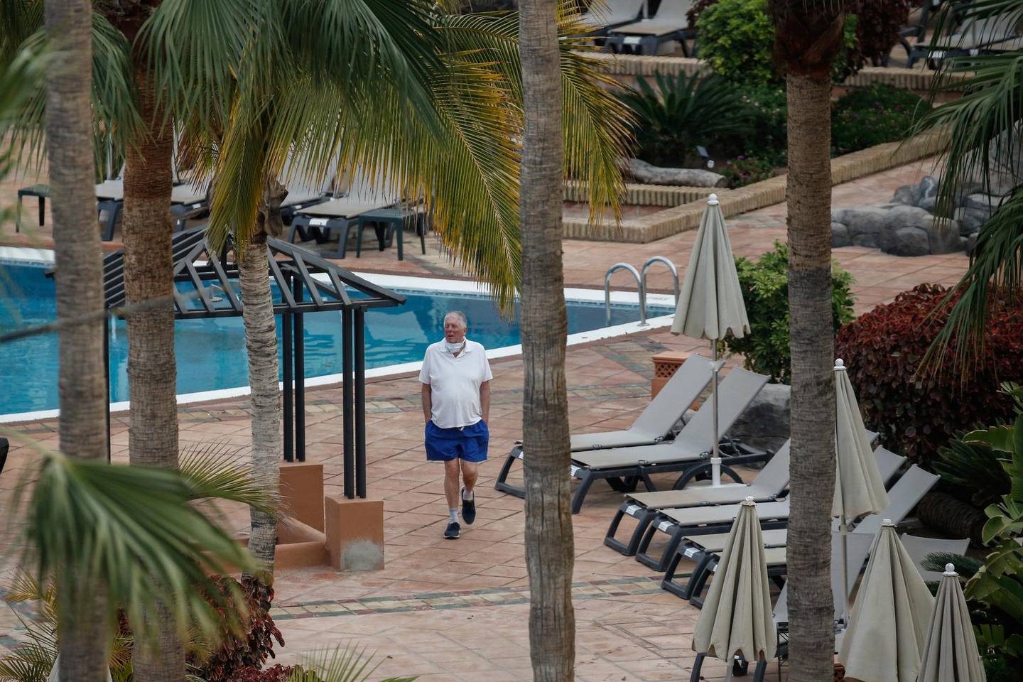 A man walks next the swimming pool of the H10 Costa Adeje Palace hotel in La Caleta, in the Canary Island of Tenerife, Spain, Thursday, Feb. 27, 2020. Spanish officials say a tourist hotel on the Canary Island of Tenerife has been placed in quarantine after an Italian doctor staying there tested positive for the COVID-19 virus and Spanish news media says some 1,000 tourists staying at the complex are not allowed to leave. (AP Photo/Joan Mateu)