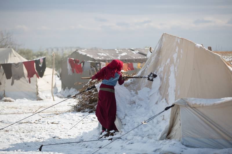 A Syrian woman scrapes snow from her destroyed tent after a snowstorm.