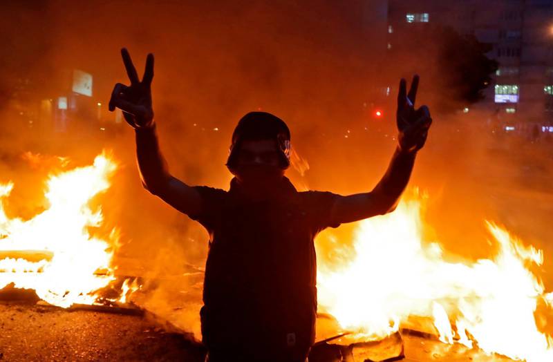 A protester flashes the victory sign in front of a burning barricade during ongoing demonstrations in Beirut. AFP