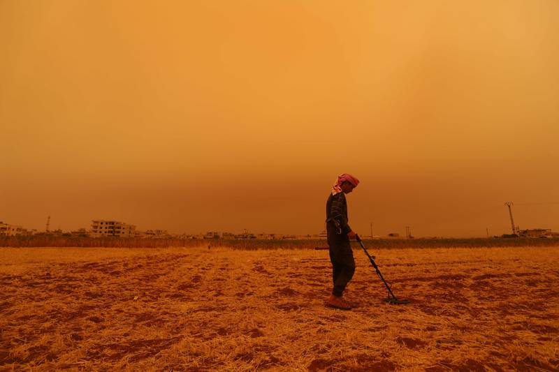 A youth uses a metal detector during a dust storm over Zardana in the countryside of Idlib province, Syria. All photos: AFP