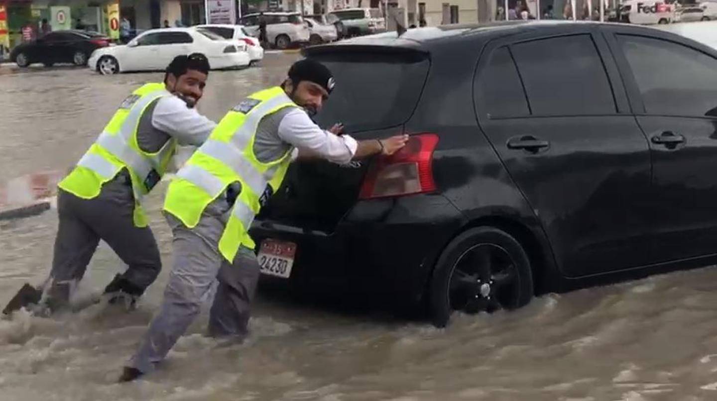 Two soaking wet police officers laugh as they help a driver through a pocket of water near RAK city. Courtesy: RAK Police