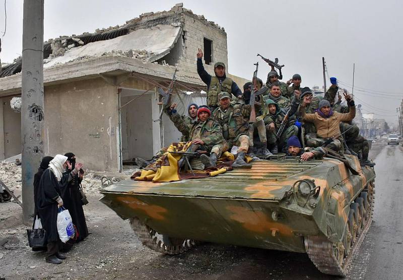 Syrian pro-government fighters drive their tank past civilians fleeing eastern Aleppo in 2016. AFP