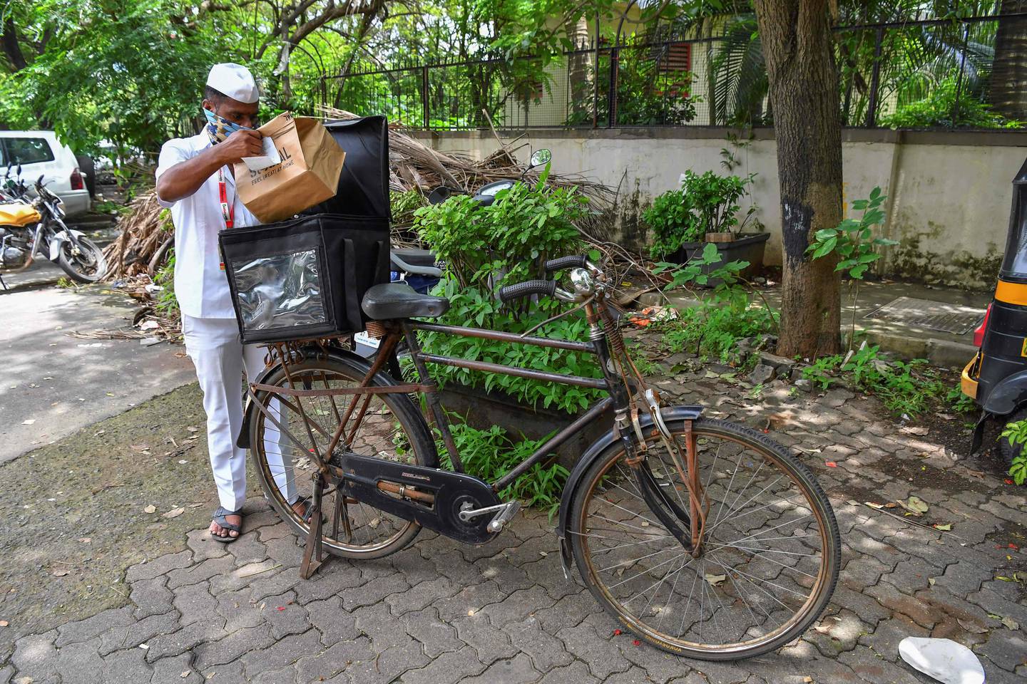 One of Mumbai's tiffin delivery men or "Dabbawallas", Pandurang Jadhav, prepares to deliver an order after collecting it from a restaurant in Mumbai. After the pandemic shut offices and put Mumbai's renowned lunchbox deliverymen out of work, the 130-year-old tiffin delivery network tied up with a restaurant chain, on June 22, 2021, in Mumbai, India. AFP