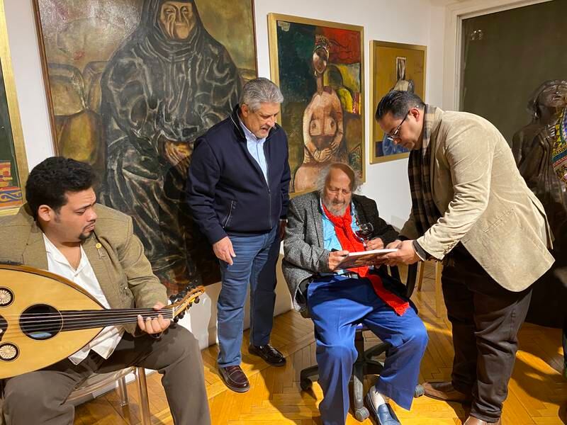 Bahgory signing books at the Art Talks exhibition opening, surrounded by his works and accompanied by an oud player. Nada El Sawy / The National