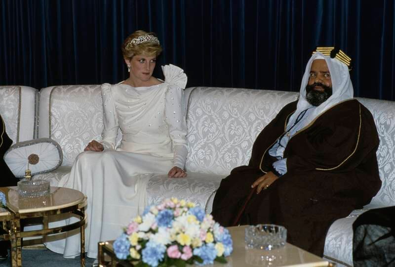 Princess Diana, wearing a white Emanuel evening dress and the Queen Mary tiara, sits beside a man at a banquet hosted by Isa bin Salman, the Emir of Bahrain, at Al Qudaibiya Palace in Manama in November 1986. 