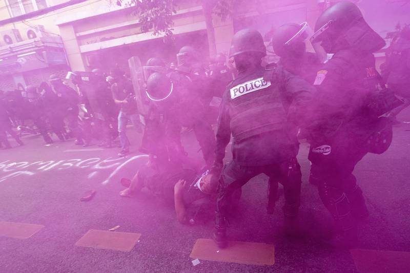 In cloud of pink smoke, police in riot gear remove a protester trying to march to the Asia-Pacific Economic Cooperation APEC summit venue, Friday, Nov.  18, 2022, in Bangkok, Thailand.  (AP Photo / Wason Wanichakorn)
