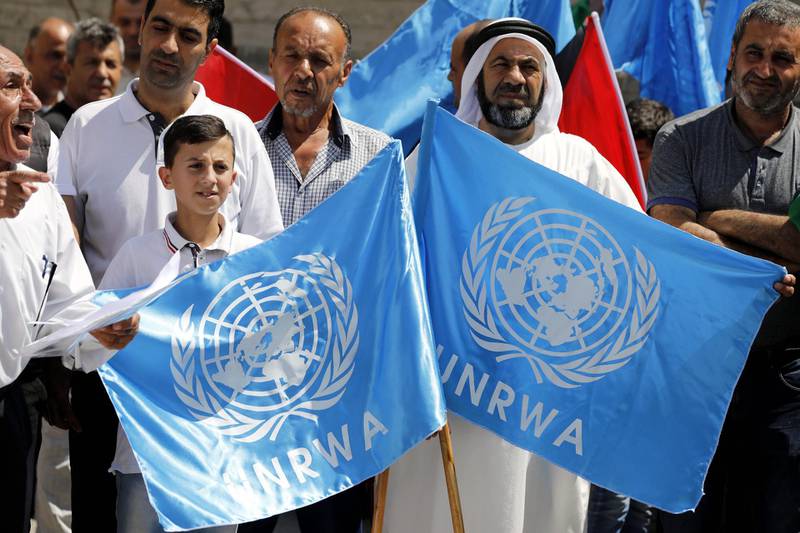 epa07005146 Palestinians hold placards alongside the United Nations (UN) and the Palestinian flags during a protest in the West Bank city of Hebron, 08 September 2018. Palestinians protest against the US cut of funds for the UNRWA (United Nations Relief and Works Agency for Palestine Refugees), and call to stand against Donald's trump plan to end the right of return for the Palestinian refugees as they say.  EPA/ABED AL HASHLAMOUN