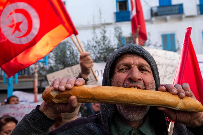 A Tunisian bites a piece of bread to protest his purchasing power during a demonstration to mark the ninth anniversary of the democratic uprising in Tunis, Tuesday, Jan.14, 2020. Tunisia is marking nine years since its democratic uprising amid deepening economic troubles and simmering anger at the revolution's unfulfilled promises. (AP Photo/Hassene Dridi)