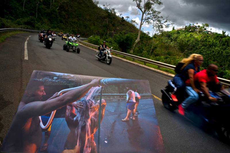 A printed photograph taken on September 28, 2017 shows people bathing on the highway after Hurricane Maria destroyed people's homes. Today motorcyclists ride by in Naranjito, Puerto Rico.