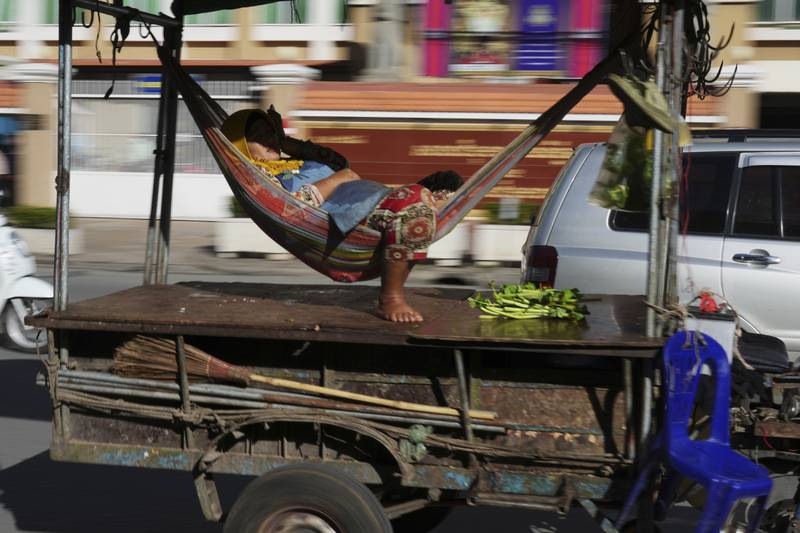 A Cambodian vendor sleeps in a hammock being carried by a motor-cart past the Phnom Penh Municipal Court building in Phnom Penh, Cambodia. AP