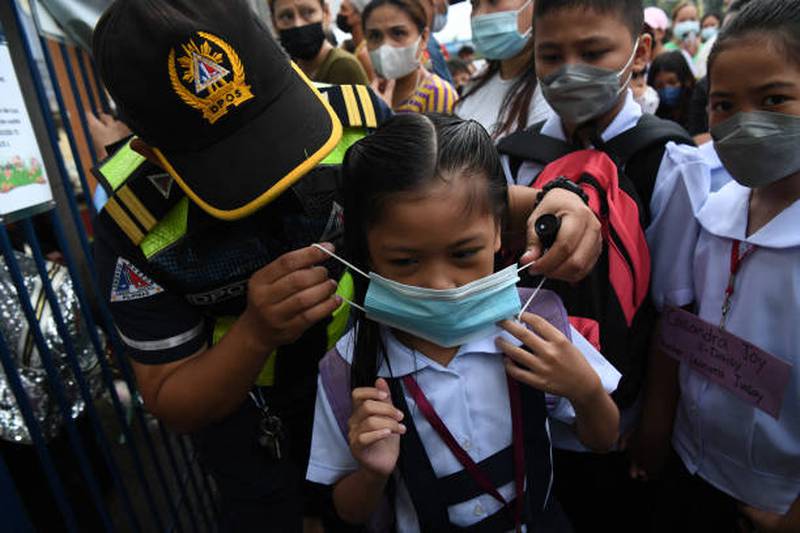 A city hall employee helps a pupil put on a face mask in Quezon city. AFP