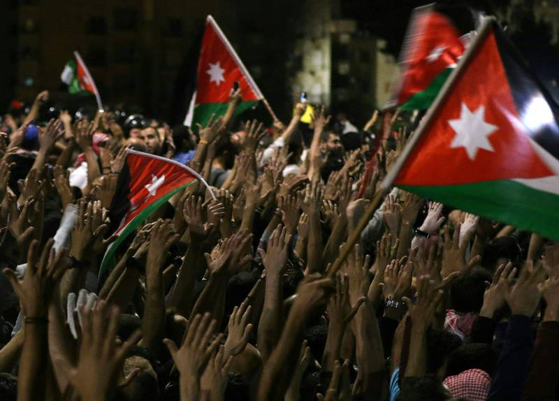 TOPSHOT - Protesters raise their hands and wave flags near members of the gendarmerie and security forces during a demonstration outside the prime minister's office in the capital Amman late on June 3, 2018. Jordan's senate met on June 3 for a special session after another night of protests across the country against IMF-backed austerity measures including a draft income tax law and price hikes. Some 3,000 people faced down a heavy security presence to gather near the prime minister's office in Amman until the early hours of Sunday morning. / AFP / Khalil MAZRAAWI
