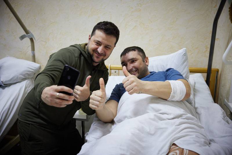 Ukrainian President Volodymyr Zelenskyy, left, snaps a selfie with a wounded man during a visit at a military hospital after fighting in the Kyiv region.AFP