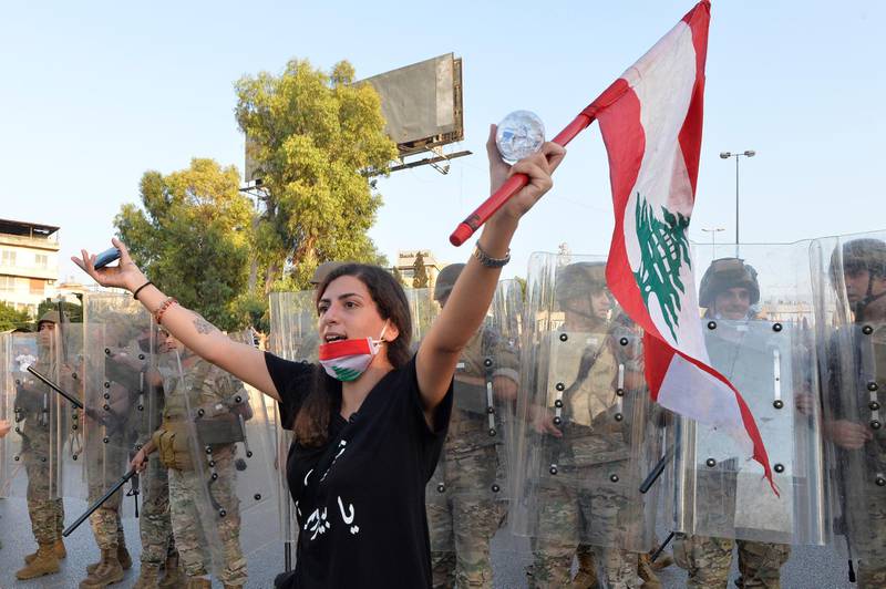 epa08665134 An anti-government protester carries a national flag as she shouts slogans in front of the Lebanese army soldiers during a protest on the road leading to the Presidential palace in Baabda, east Beirut, Lebanon, 12 September 2020. Hundreds of anti-government protesters gather outside the Presidential palace to protest against politicians, security and judicial officials, many of whom knew about the storage of the chemicals that exploded in Beirut's port on 04 August, and did nothing.  EPA/WAEL HAMZEH