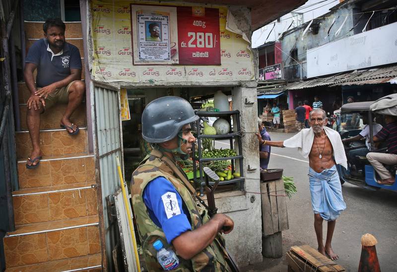 Sri Lankans stand near a roadside shop as a Naval soldier stand near the damaged St Anthony's Church, in Colombo. AP Photo
